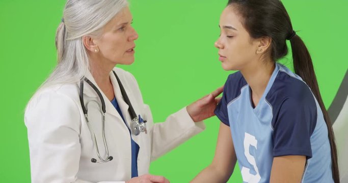 Young concussed soccer player is check for dilated pupils by her physician on green screen. On green screen to be keyed or composited. 