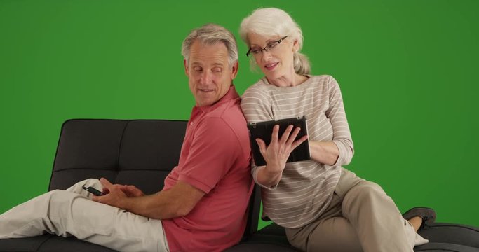 Senior couple using devices on couch at home on green screen. On green screen to be keyed or composited. 