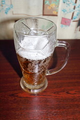 White beer foam in a glass on a dark table in front of a window
