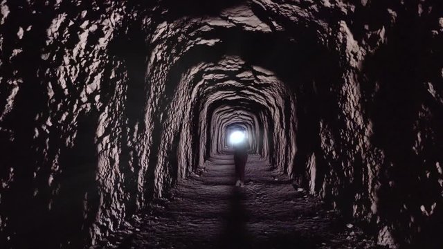 Silhouette of woman walking inside a tunnel towards the light. 4k