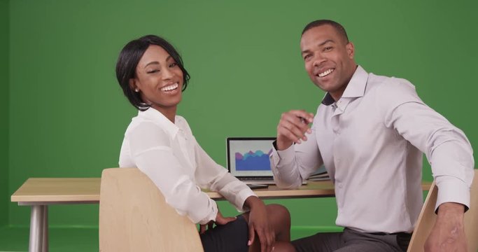 Happy smiling African American business coworkers sitting at desk together on green screen. On green screen to be keyed or composited. 