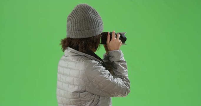 Black millennial girl takes pictures with her mirrorless camera in winter clothes on green screen. On green screen to be keyed or composited. 