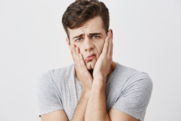 Shocked stunned emotional man keeps hands on cheeks, being troubled to listen advices of his...