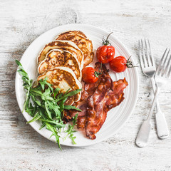 Traditional american breakfast - crispy bacon, pancakes with maple syrup, roasted tomatoes, arugula. On a light background, top view