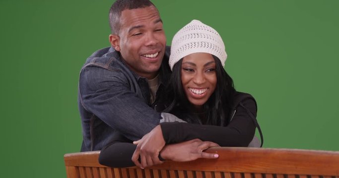 Couple sitting on a bench together looking at the view laughing and smiling on green screen. On green screen to be keyed or composited. 