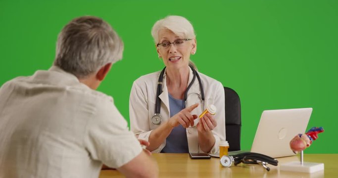 Senior doctor prescribing medication to elderly patient on green screen. On green screen to be keyed or composited. 