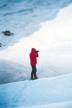 A man in snowshoes takes pictures of mountains.