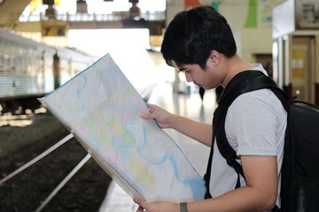 Handsome young Asian tourist with a bag looking at map in train station with copy space background.