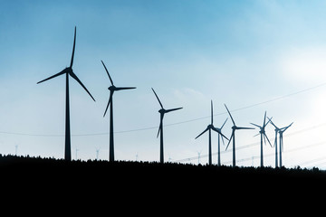 Black Silhouette of windturbines energy generator on blue sky at a wind farm in germany