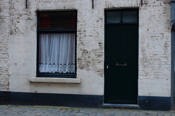Typical medieval building facade in Europe. Green wooden door and window with white curtain. White vintage brick house in Belgium, Brugge (Bruges). Medieval architecture. Street building exterior. 