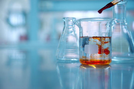 clear glass beaker with orange drop solution in science laboratory background