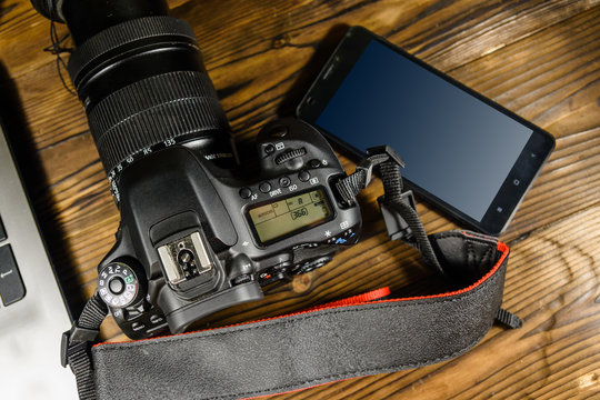 Modern DSLR camera, smartphone and laptop on wooden table. Top view
