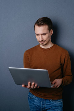 Young man holding laptop against dark wall