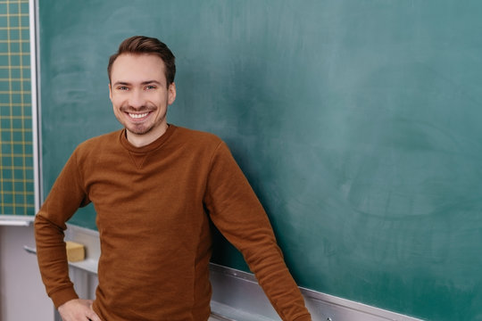 Young smiling man standing by blackboard