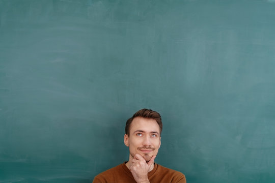 Young thoughtful man standing against blackboard
