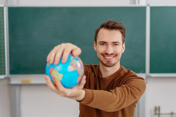 Young smiling man holding globe against blackboard
