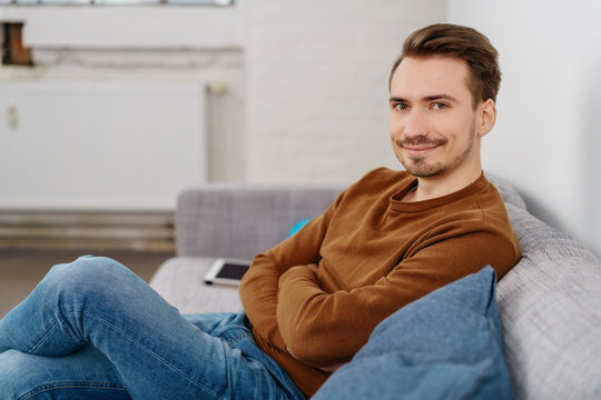 Young smiling man sitting on sofa at home