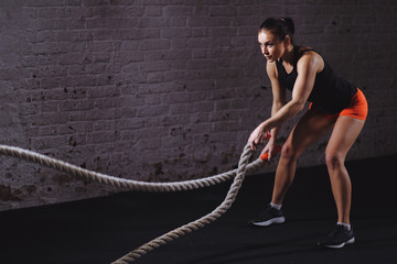 Woman training with battle rope in cross fit gym