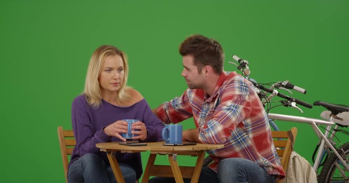 Millennial white couple sitting at a nice caf_ table drinking coffee together on green screen. On green screen to be keyed or composited. 