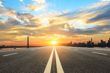 Empty asphalt road and city skyline at sunset