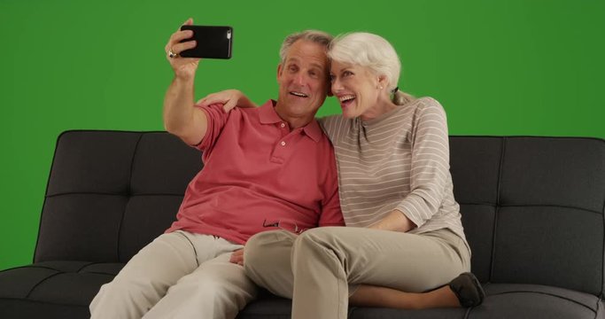 Cute senior couple taking a selfie with smartphone at home on green screen. On green screen to be keyed or composited. 