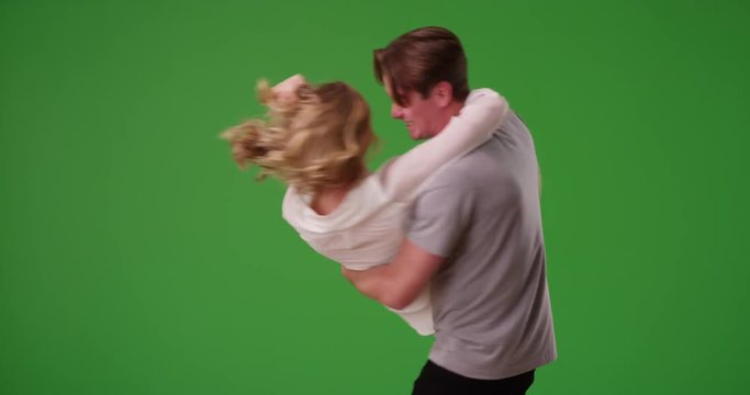 Smiling playful male picking up girlfriend in his arms and spinning her around on green screen. On green to be keyed or composited. 