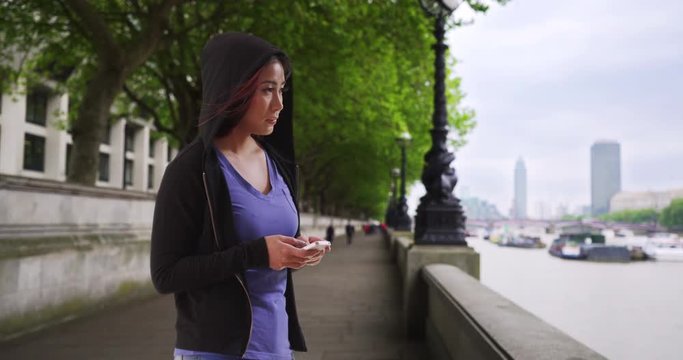 Japanese female in black hoodie texting on mobile phone by River Thames