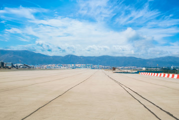 Beautiful landscape view of runway, airstrip in the airport terminal ready for airplane landing or taking off with blue cloudy sky and mountains at background. Travel aviation future concept.