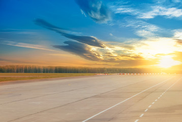 Beautiful evening landscape of runway, airstrip in the airport terminal ready for airplane landing or taking off with dramatic cloudy sunset background. Travel aviation future concept at golden hour.