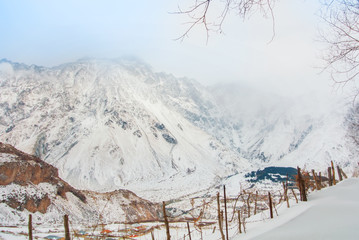 Panoramic aerial top view to winter Caucasian mountains covered with snow, ice and glaciers near Stepantsminda village against the stormy cloudy foggy sky, Georgia. Broken wooden fence at foreground.