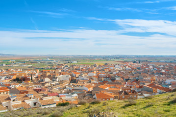 Aerial panoramic view over the orange tile roofs to a small spanish town village Consuegra (Castilla - La Mancha) on sunny day with colorful farm country landscape with fields and parcels.