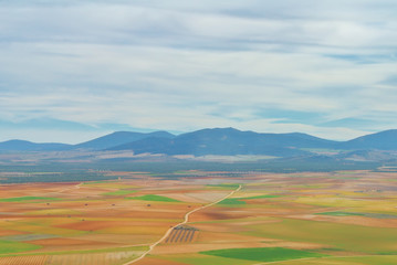 Abstract aerial panoramic top view of a country farm agricultural landscape, a road and colorful geometric shapes of brown, orange and green spring fields parcels and blue mountains at the background.