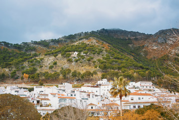 Aerial panoramic view over the roofs of a small touristic white-washed village at Malaga province (Andalusia, Spain) and mountains at the background on winter cloudy day.