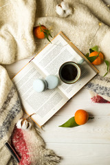 Top view blue coffee cup on the open book with winter essentials clementine mandarin, plaid and glowing christmas lights on the white wooden window sill. Christmas, holiday morning comfort concept