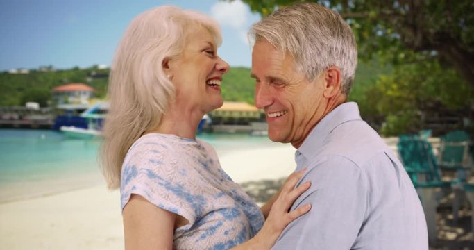 Cheerful elderly couple standing at the beach talking and laughing