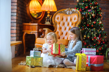 Fototapeta na wymiar beautiful sisters sit on the floor near the tree and give each other presents and have fun.