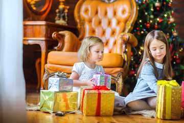 Fototapeta na wymiar Christmas morning, two sisters open gifts sitting on the floor near a festive Christmas tree.