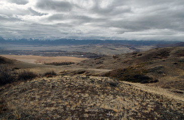 Dramatic dark desert steppe on a highland mountain plateau with ranges of  snow peaks on a horizon storm skyline Kurai Altai Mountains Siberia Russia