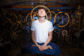 Fototapeta na wymiar Young man is practicing yoga in garage with many bicycles behind him