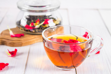 A cup of tea, in the background of a bank with a black herbal floral tea on a white wooden table.