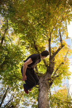 Young man doing a side flip or somersault while practicing parkour on the street with a tree in the background.  