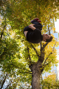 Young man doing a side flip or somersault while practicing parkour on the street with a tree in the background.  