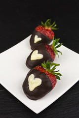 red strawberry dipped in dark chocolate decorated with heart of white chocolate
