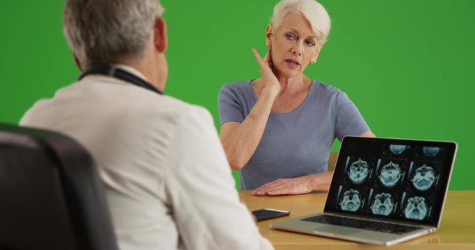 Elderly woman patient telling her doctor about the pain in her neck on green screen. On green screen to be keyed or composited. 