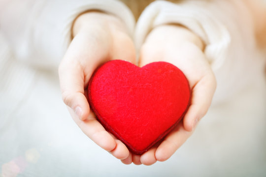 Red heart in hands of the little girl. Symbol of love and family.Valentines day card. Mother's day. Backgrounds for social posters. Selective focus.