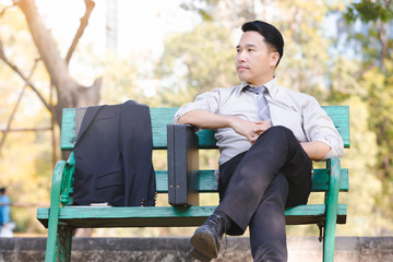 Obraz premium Portrait asian business man sit on a green wooden chair relaxation in park