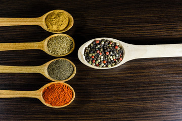 Spoons with the different spices on dark wooden table. Top view
