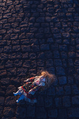 Vintage china doll lying in cobblestone street backlit by low autumn sunlight.