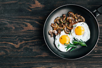Vegetarian breakfast with fried eggs and mushrooms decorated with a rosemary sprig in a frying pan on a wooden table