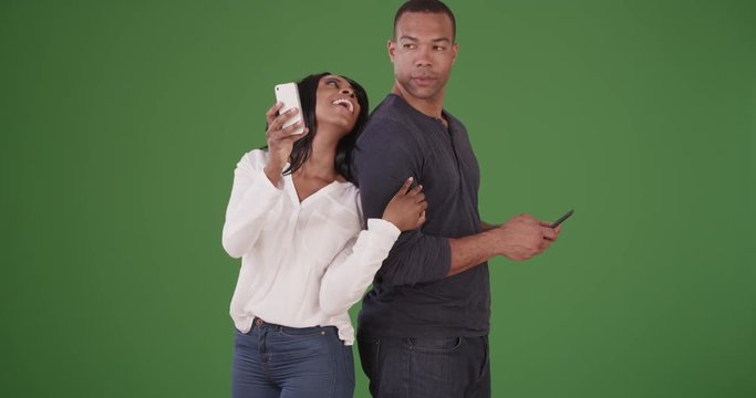 Couple standing back to back texting on cell phones on green screen. On green screen to be keyed or composited. 